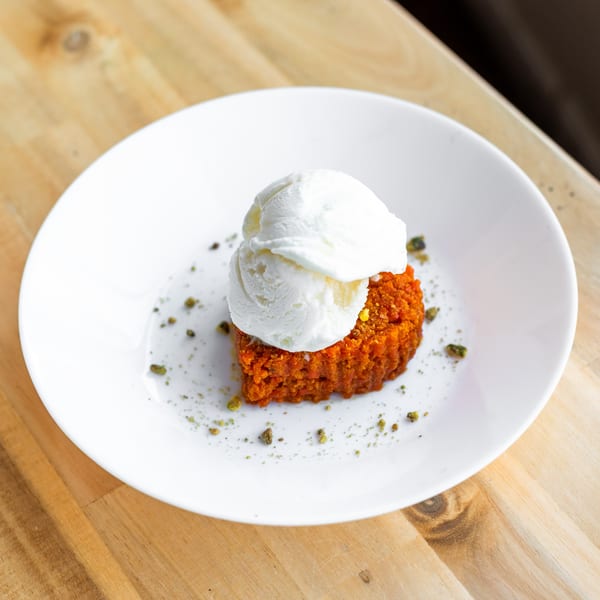 Gajar Halwa, an Indian carrot pudding, topped with a scoop of vanilla ice cream on a white plate.