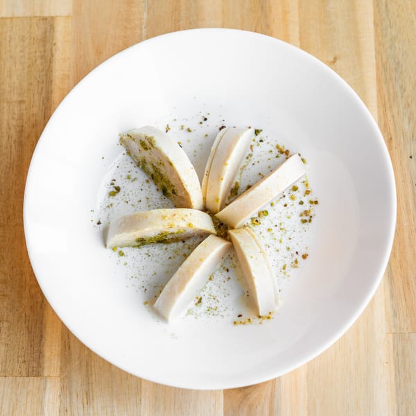 Slices of Indian Kulfi dessert, garnished with green pistachio powder, arranged on a white plate.