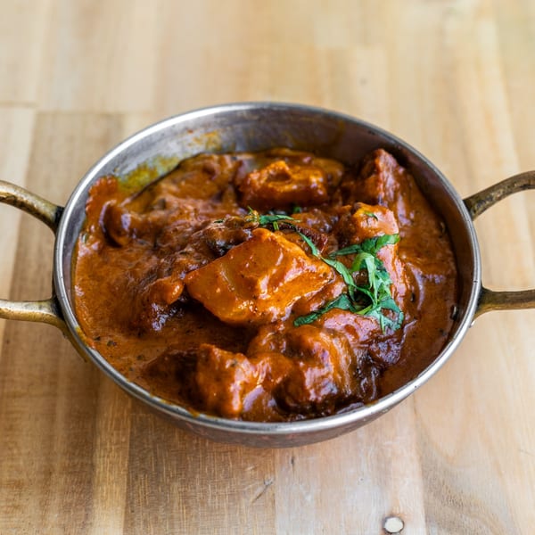 Bombay Palace's chicken tikka masala, a rich orange curry with chicken pieces, garnished with cilantro in a metal bowl.