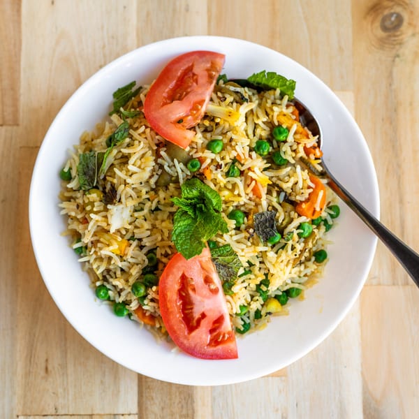Bombay Palace's vegetable biryani, a flavorful Indian rice dish with peas, carrots, and mint, garnished with tomato slices.
