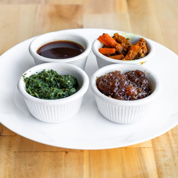 Four small white bowls of Indian chutneys and pickles on a white plate.