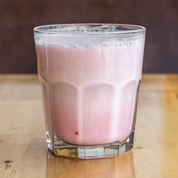 A glass of pink strawberry lassi, a traditional Indian yogurt drink, on a wooden table.