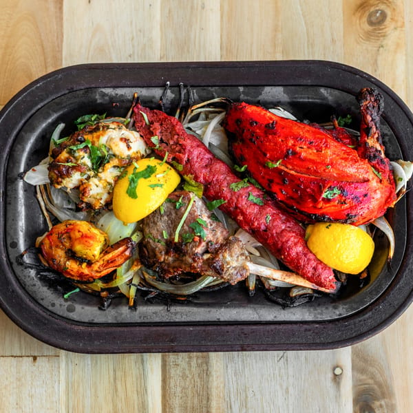 Bombay Palace's sizzling tandoori platter with chicken, lamb, shrimp, and lemon on a black tray.