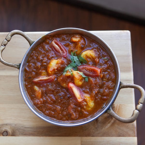 Bombay Palace's Indian curry with shrimp, tomatoes, and cilantro in a metal serving bowl.