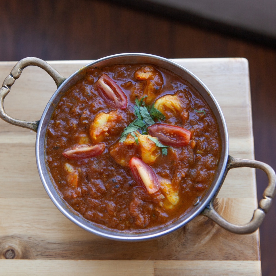 Bombay Palace's Indian curry with shrimp, tomatoes, and cilantro in a metal serving bowl.